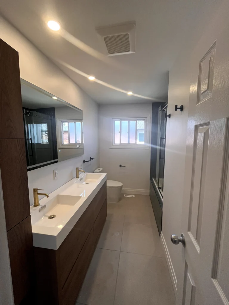 Modern renovated bathroom with double vanity, gold faucets, tiled flooring, and ceiling exhaust fan for moisture control and mold prevention