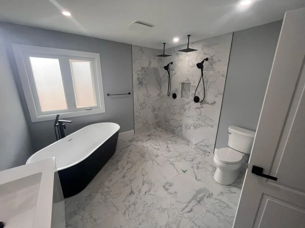 Modern bathroom renovation featuring a freestanding black and white bathtub, large walk-in curbless shower with dual rainfall showerheads, marble-look tiles, and a wall-mounted toilet—part of a complete 3-week remodel in the Greater Toronto Area.