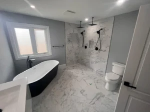 Modern bathroom renovation featuring a freestanding black and white bathtub, large walk-in curbless shower with dual rainfall showerheads, marble-look tiles, and a wall-mounted toilet—part of a complete 3-week remodel in the Greater Toronto Area.